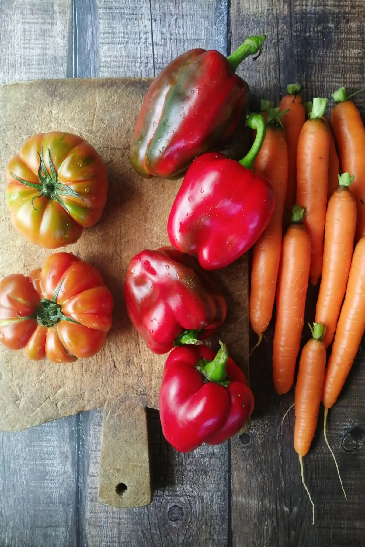 Some peppers and carrots sit on a chopping board.