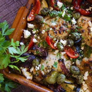 A pan of Greek chicken thighs with roasted vegetables.