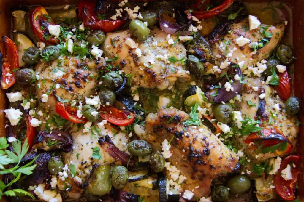 A pan of Greek chicken thighs with roasted vegetables.