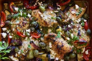 A pan of Greek chicken thighs with roasted vegetables.