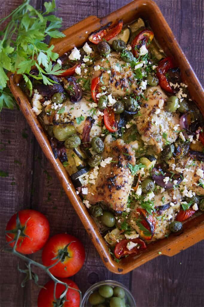 A pan of Greek chicken thighs with roasted vegetables.