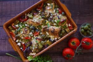 A pan of Greek chicken thighs with roasted vegetables.