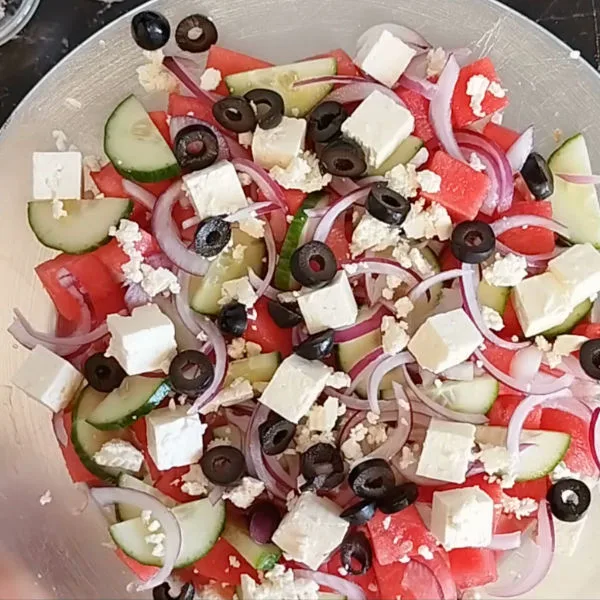 black olive and feta cheese are added to a plate of watermelon salad.