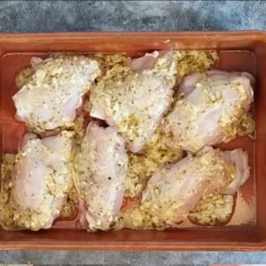 Chicken thighs in a deep pan with a marinade spooned over them.