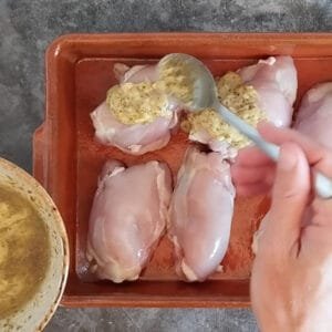 Chicken thighs in a deep pan with a marinade spooned over them.