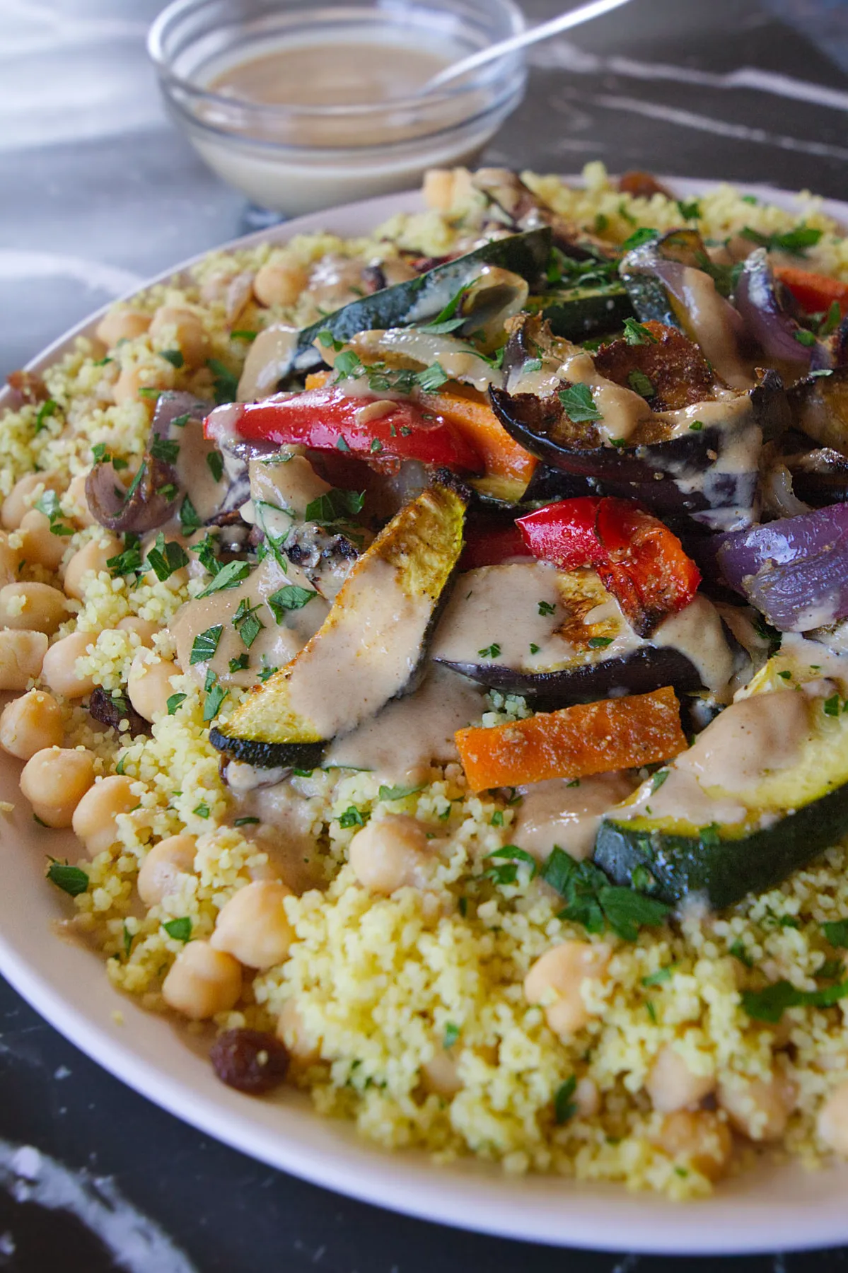A large plate of Moroccan couscous with roast veggies and drizzled with a tahini dressing.