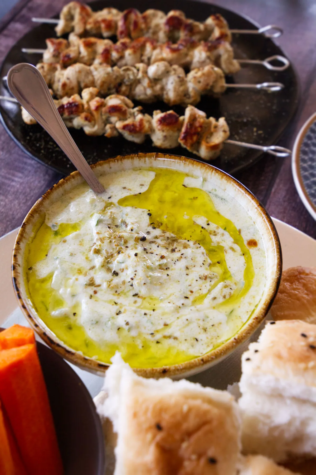 a bowl of creamy tzatziki sits eside some grilled chicken souvlaki skewers