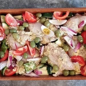 A pan of uncooked vegetables with chicken thighs and marinade.