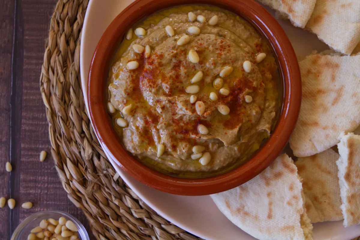 a bowl of baba ganoush garnished with olive oil and pine nuts