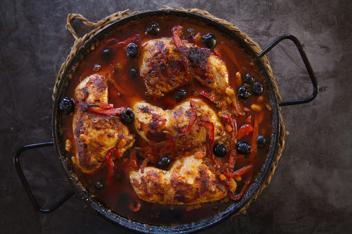 A large pan of chicken in a rich red bravas sauce