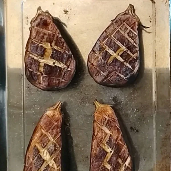 Cooked eggplant halves sit on a baking tray.