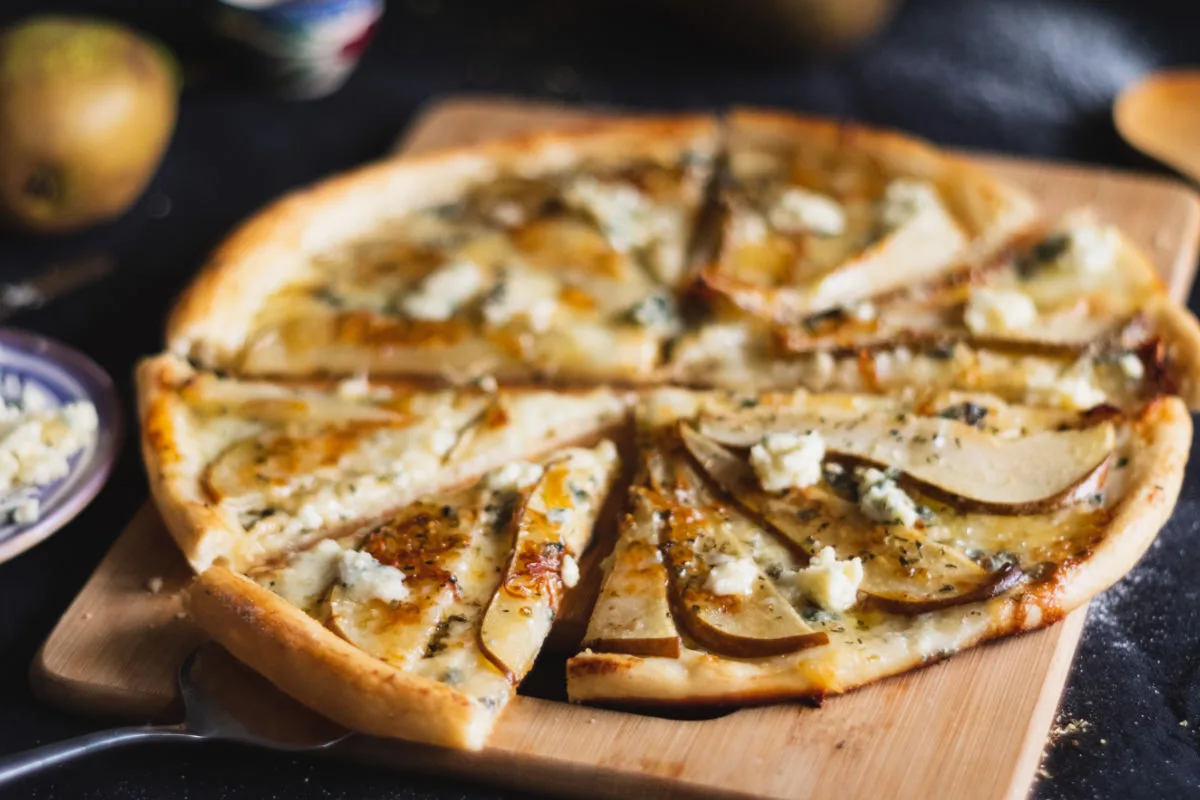 A gorgonzola and pear pizza sits sliced waiting to be served.