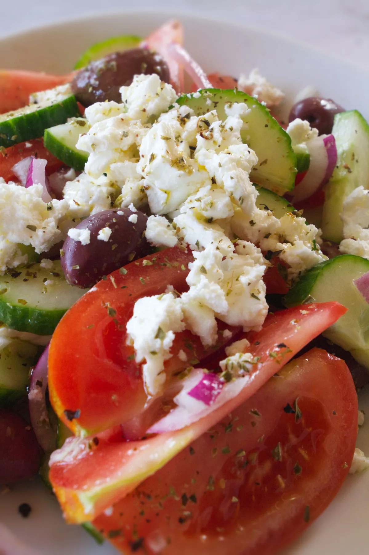 A bowl of Greek salad is garnished with some crumbled feta cheese.