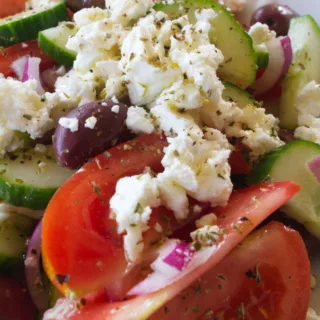 A bowl of Greek salad is garnished with some crumbled feta cheese.