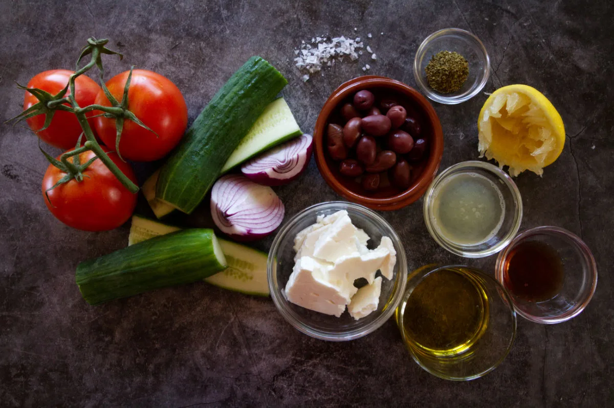 Ingredients for making Greek salad are laid out on a counter top.