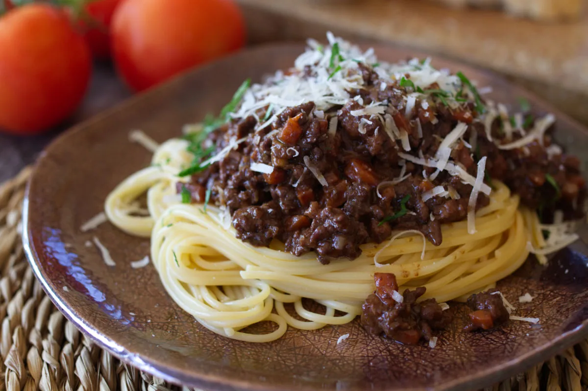 A plate of spaghetti and bolognese sauce topped with parmesan and some chopped parsley.