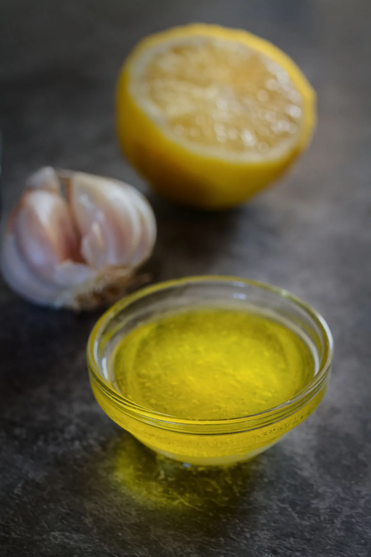 A wedge of lemon sits beside some olive oil and a clove of garlic.