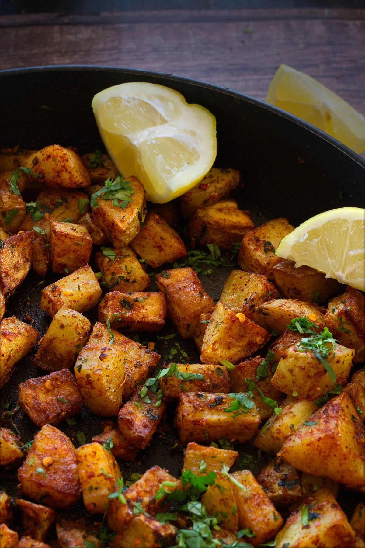 A pan or batata harra with some fresh chopped cilantro and lemon wedges.