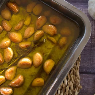 A pan of garlic cloves slow cooked in oil with some rosemary.