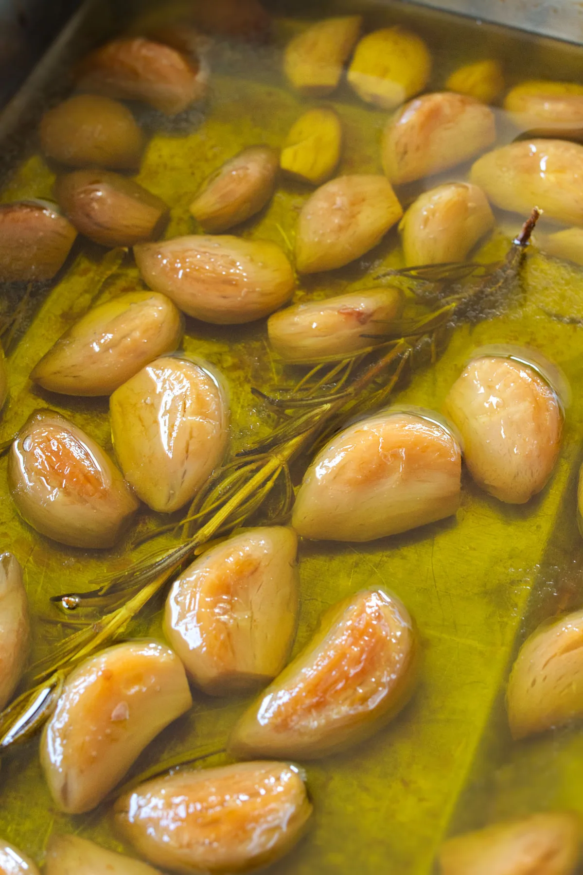 A pan of garlic cloves slow cooked in oil with some rosemary. 