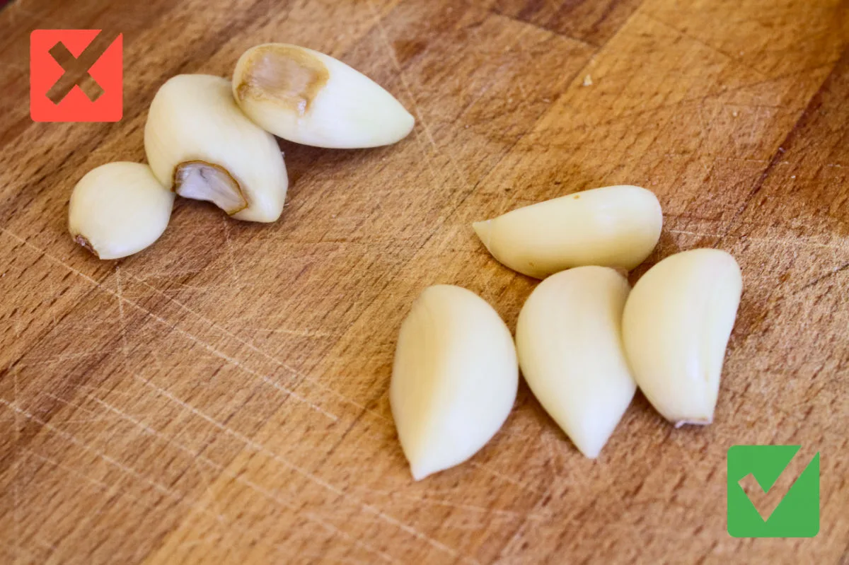 A few healthy garlic cloves sit next to some cloves with rot. 