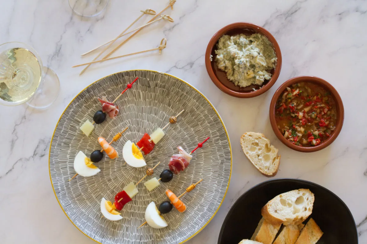 Some banderillas are served on a colorful plate beside some other tapas and dips.