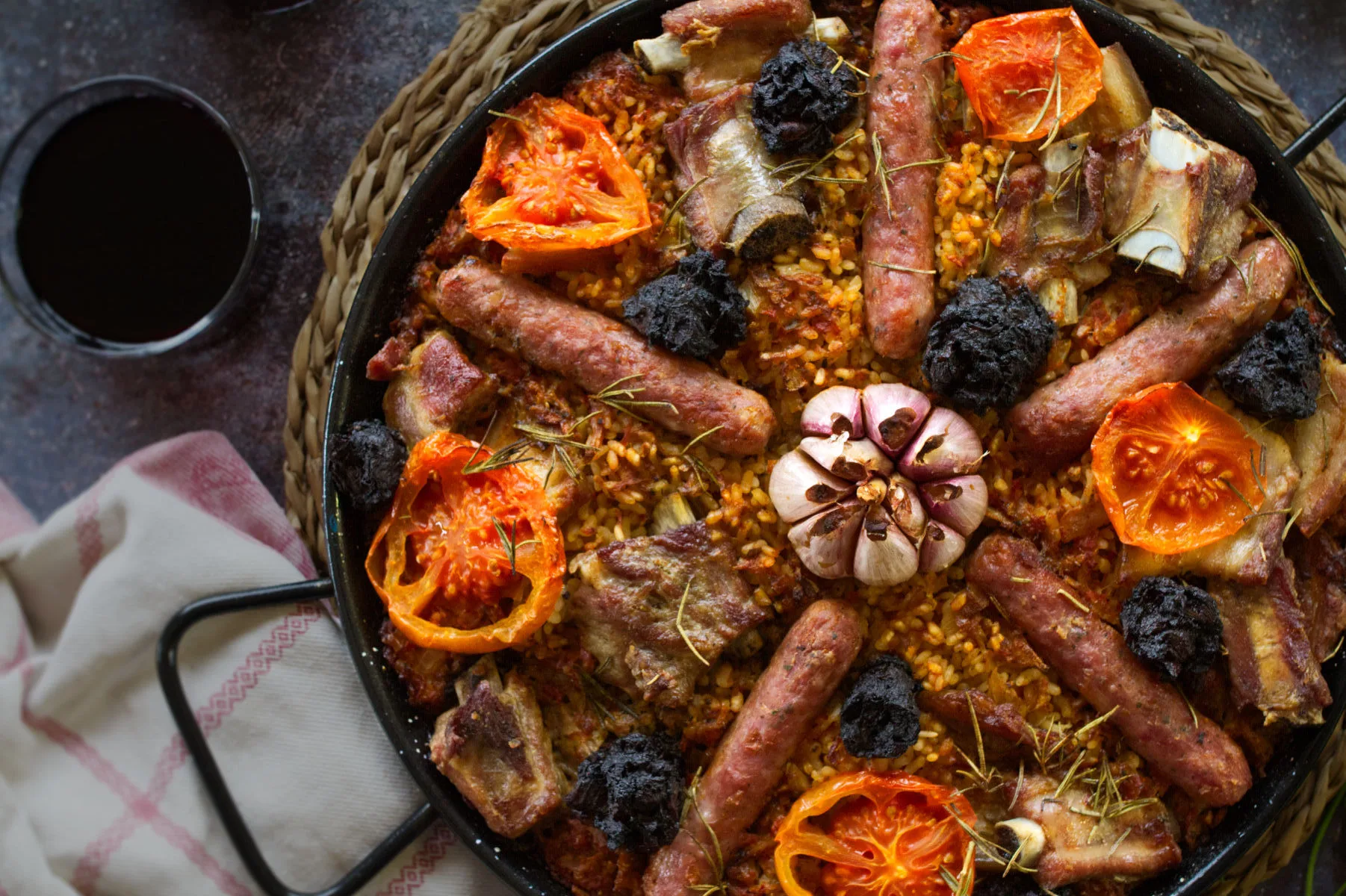 a large pan of arroz al horno sits beside some glasses of red wine.