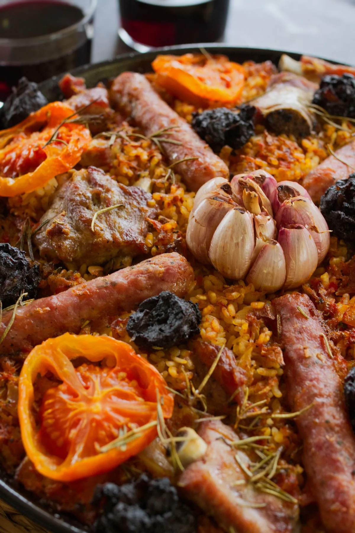 a large pan of arroz al horno sits beside some glasses of red wine.