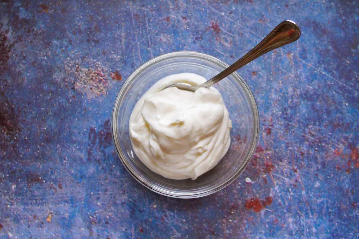 A small bowl of yogurt sits with a spoon on a blue countertop.