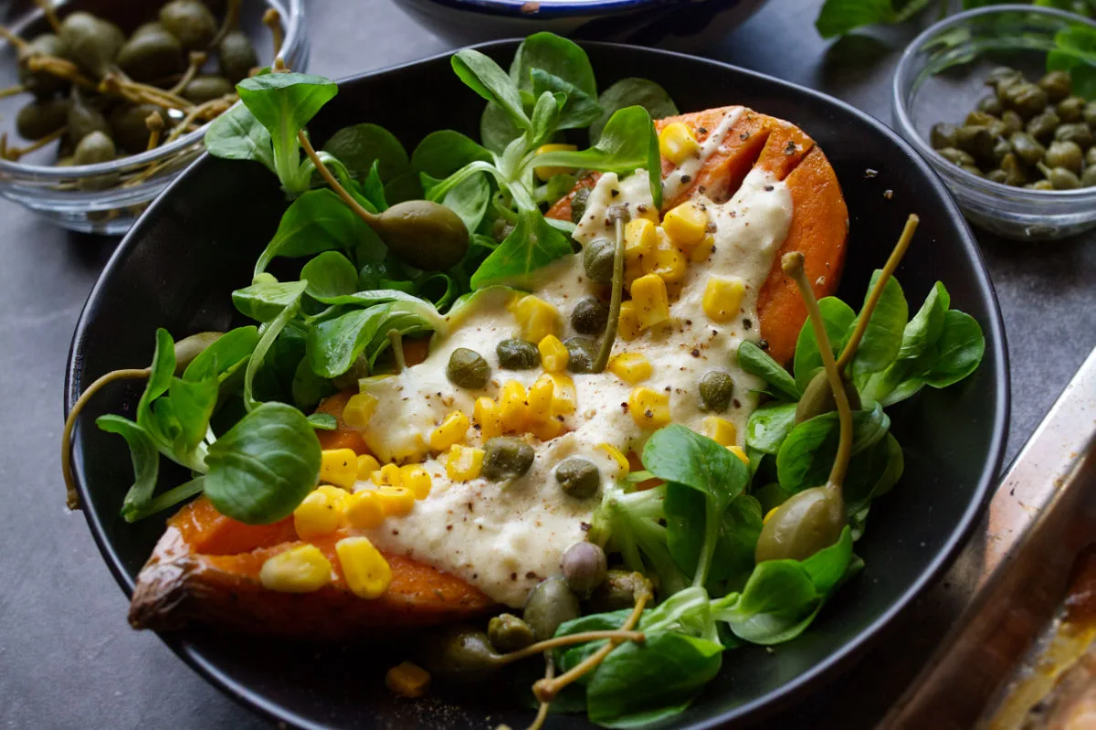 A large baked sweet potato topped with salad and a yogurt sauce.