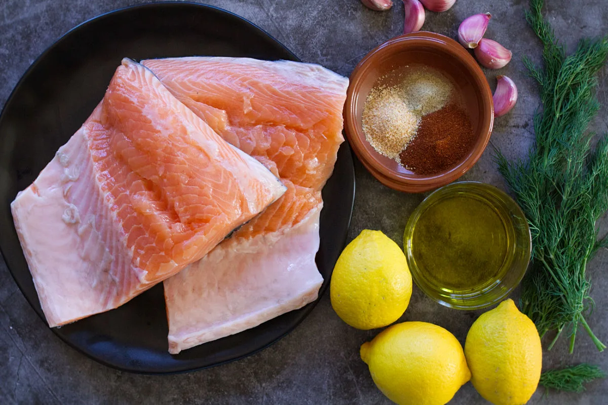 two large salmon fillets sit beside garlic, dill, lemons, and spices.