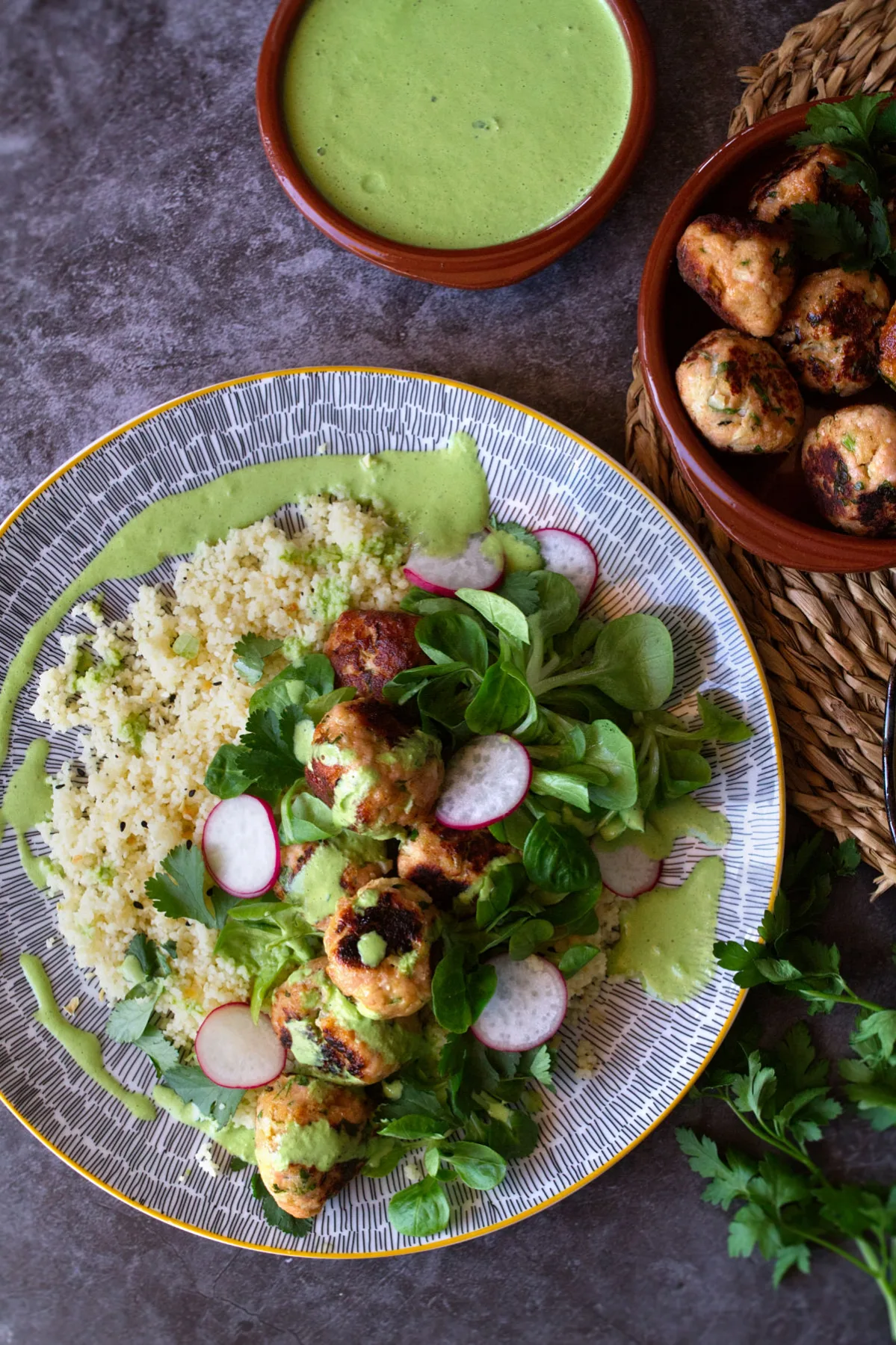 a large plate of couscous with chicken meatballs and a green yogurt sauce