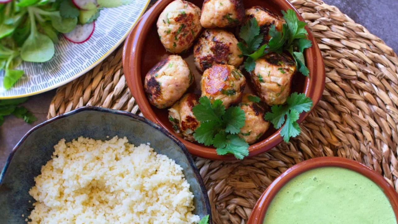 Chicken meatballs sit beside some couscous and green yogurt dressing.