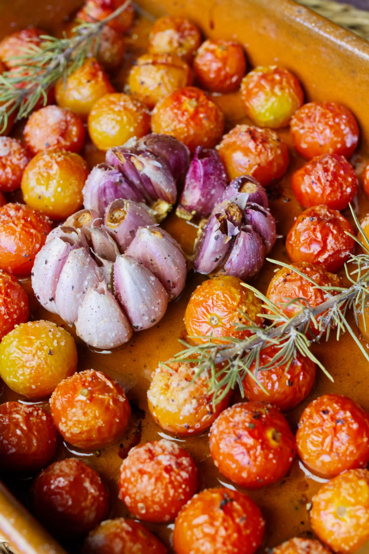 A dish of oven baked cherry tomato confit with garlic and a sprig of rosemary.