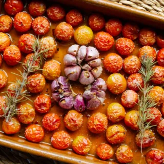 A dish of oven baked cherry tomato confit with garlic and a sprig of rosemary.