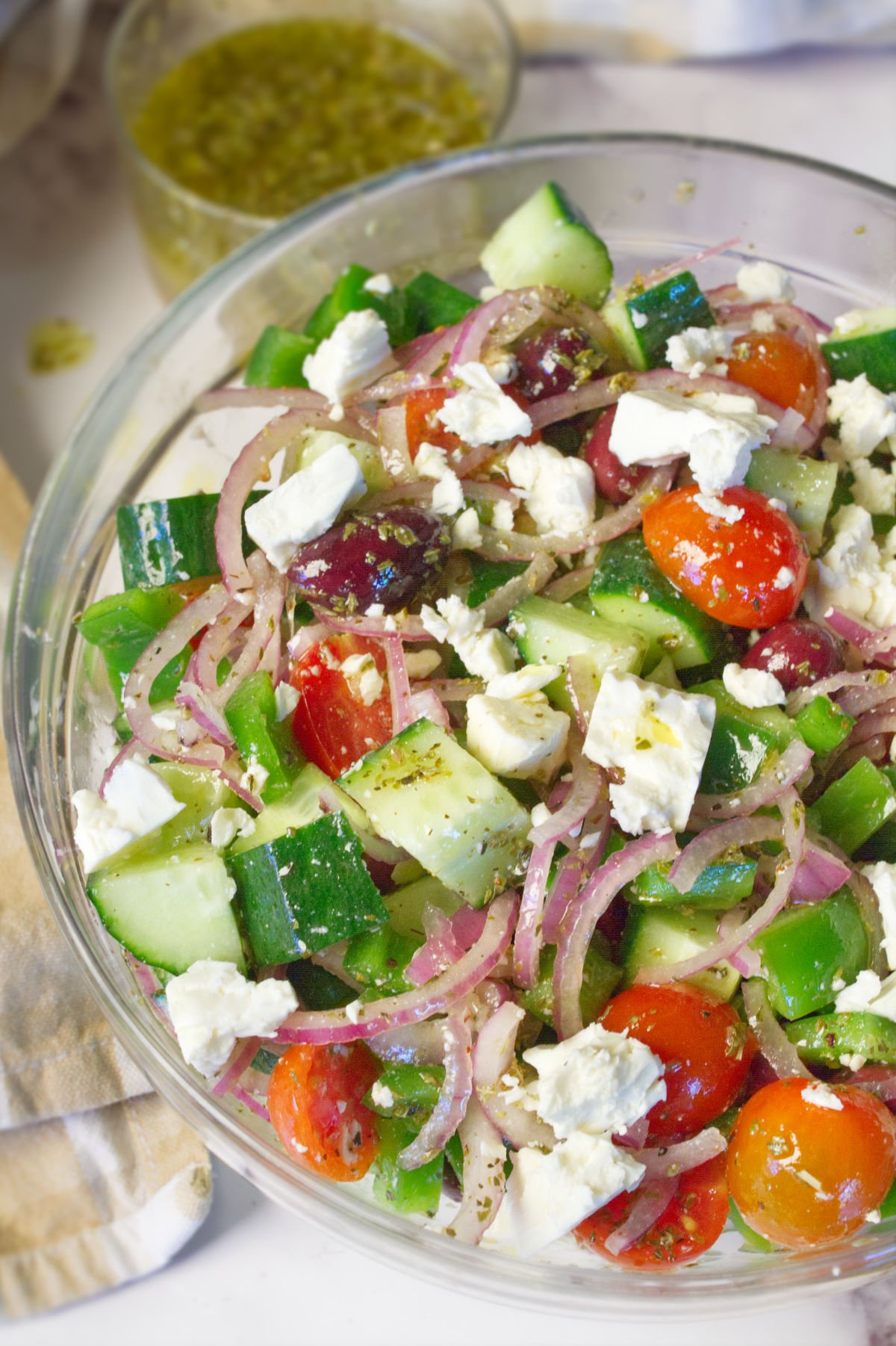 A large bowl of Horiatiki Greek Salad sits beside some salad dressing.