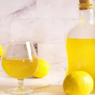 A large bottle of limoncello sits beside a small glass serving.