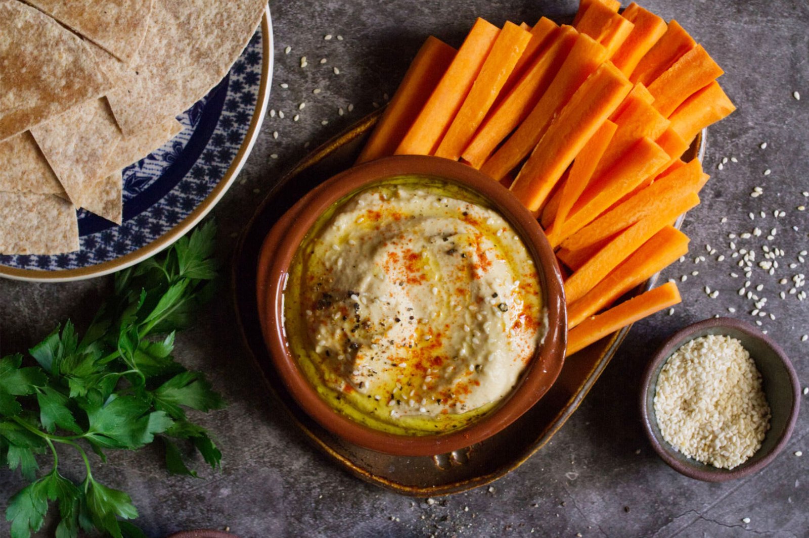 A small bowl of Mediterranean hummus beside some bread and carrot sticks.