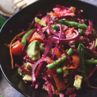 A bowl of beet and quinoa salad beside some fresh mint leaves and limes.
