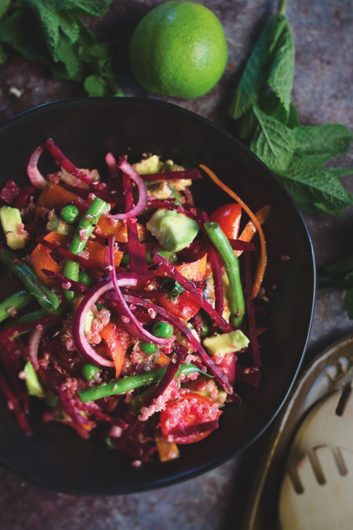 A bowl of beet and quinoa salad beside some fresh mint leaves and limes.