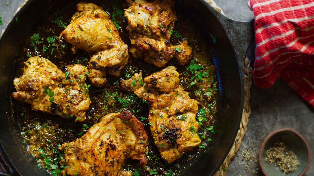 A skillet of Mediterranean chicken sits with some fresh chopped parsley as garnish.