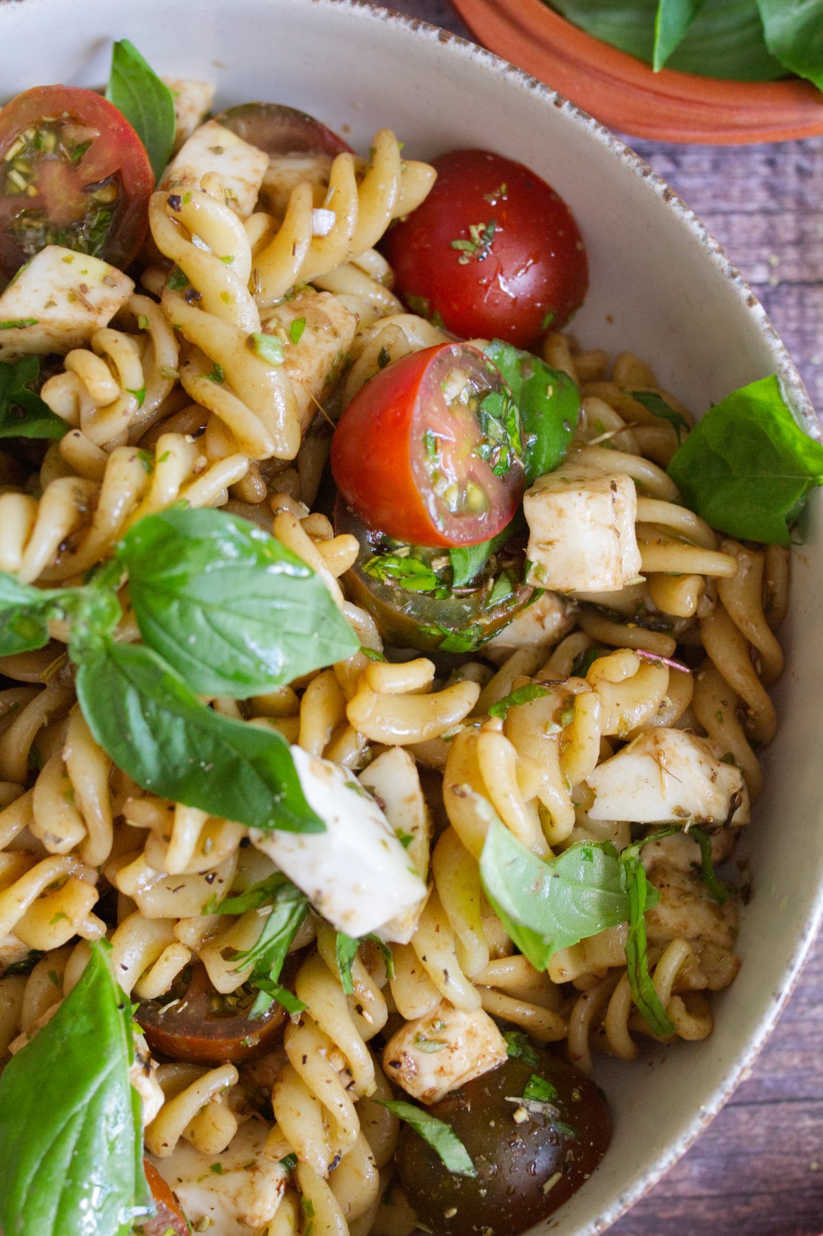 A bowl of Caprese pasta salad sits garnished wirh fresh basil leaves.