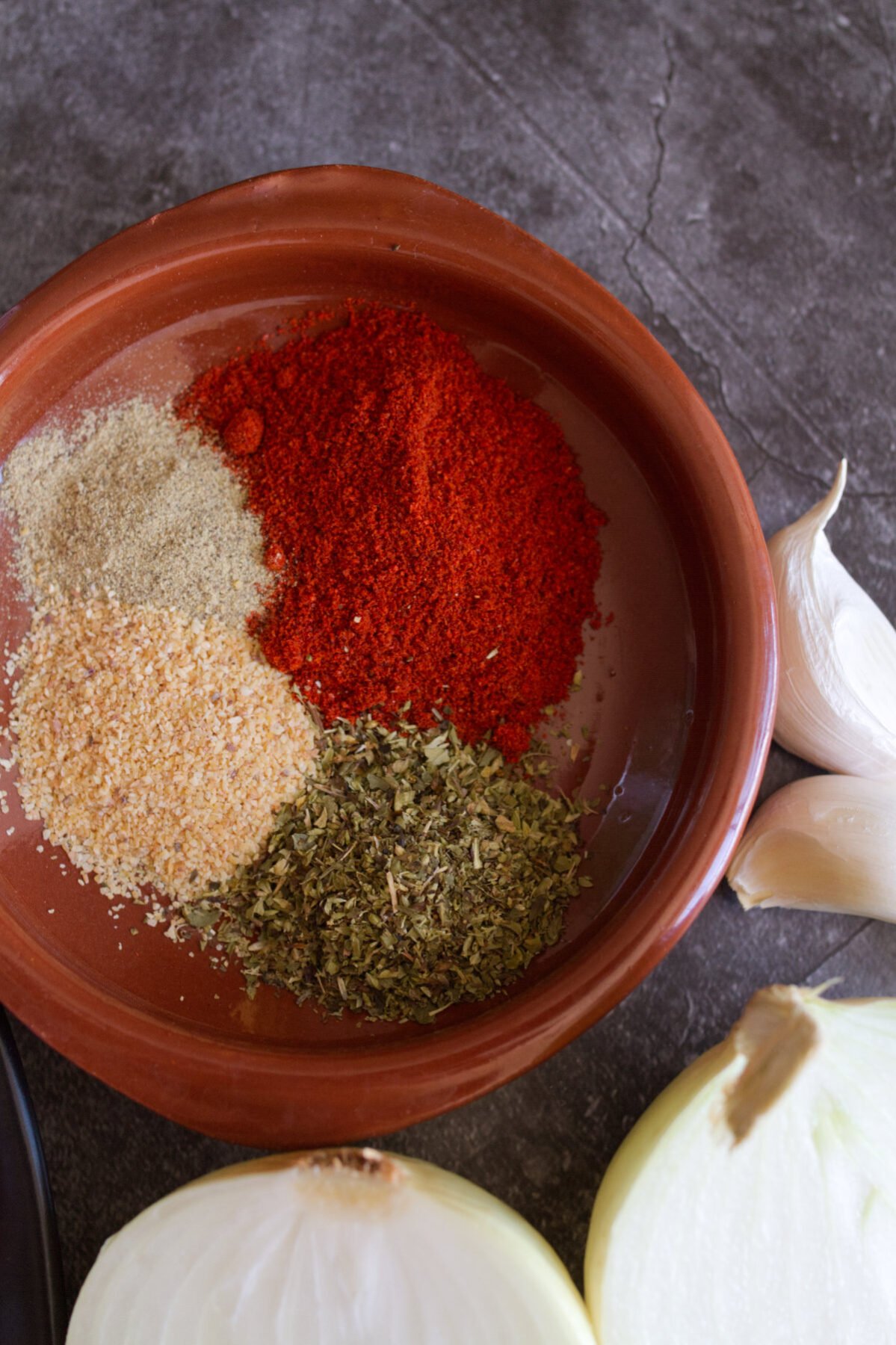 herbs-and-spices-pin - happymediterranean.com Some Spanish paprika, oregano, garlic powder and seasoning sit in a small bowl.