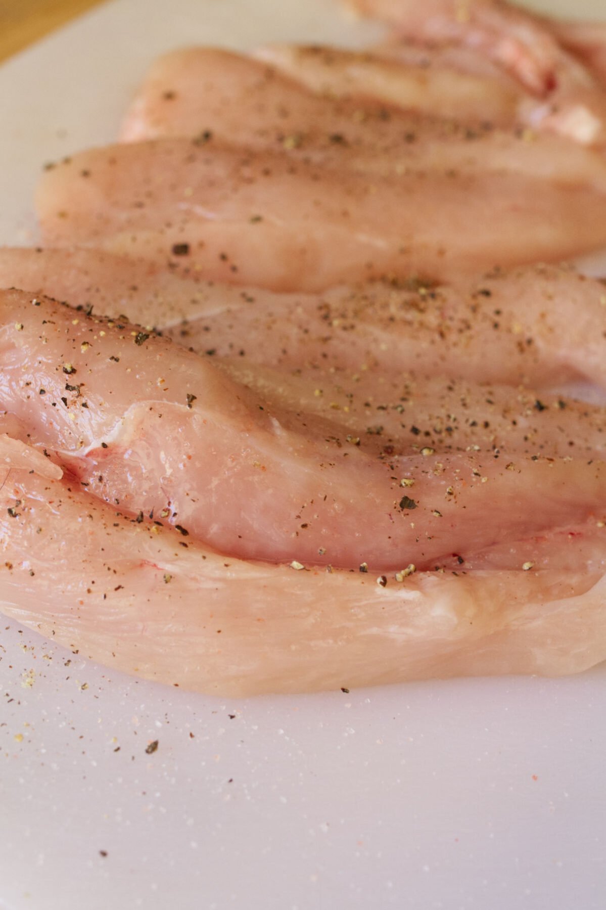 thin slices of seasoned chicken breast sit on a chopping board. 