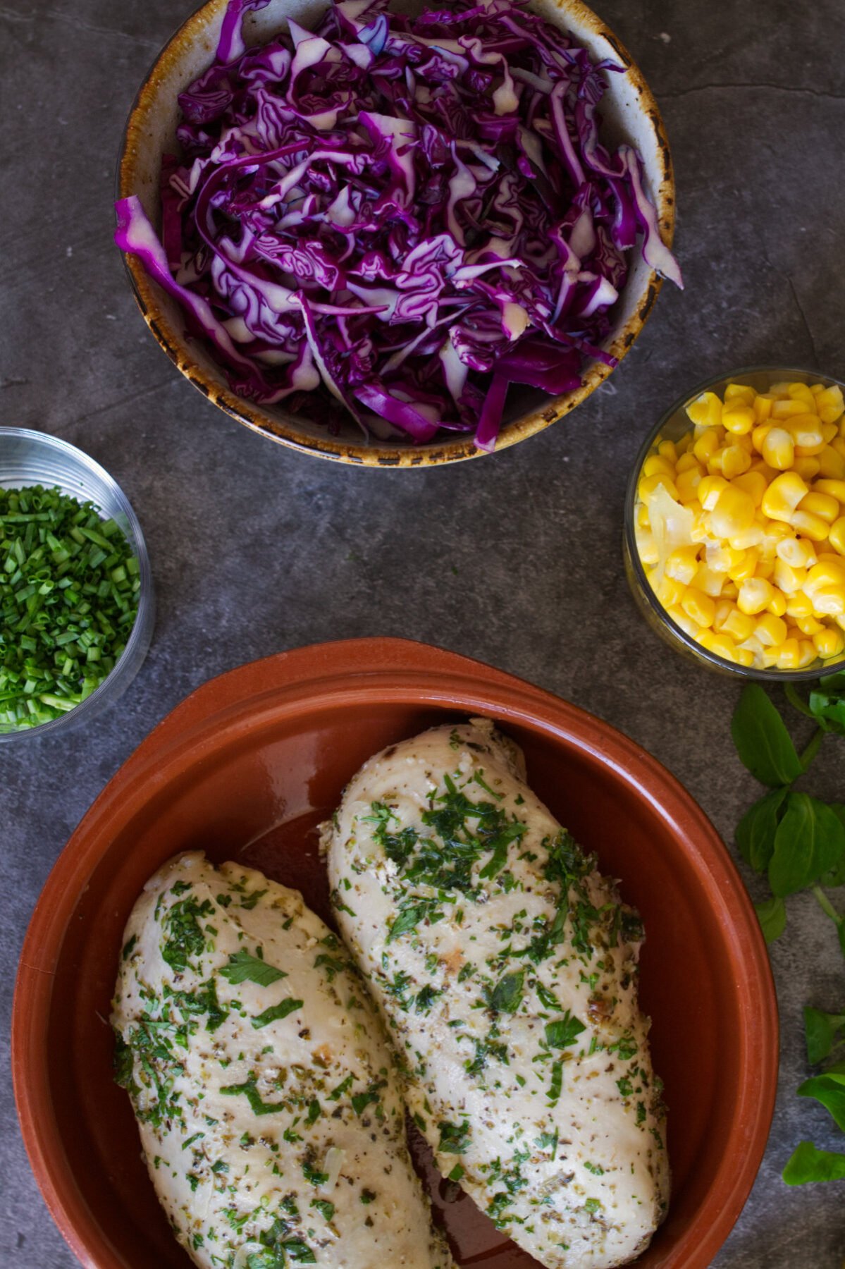 two cooked chicken breasts sit beside some salad ingredients.