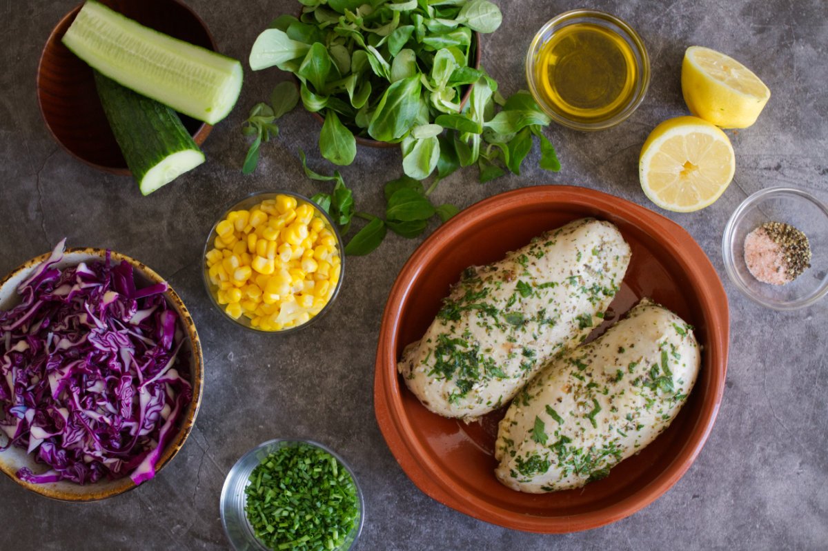 two cooked chicken breasts sit beside some salad ingredients. 