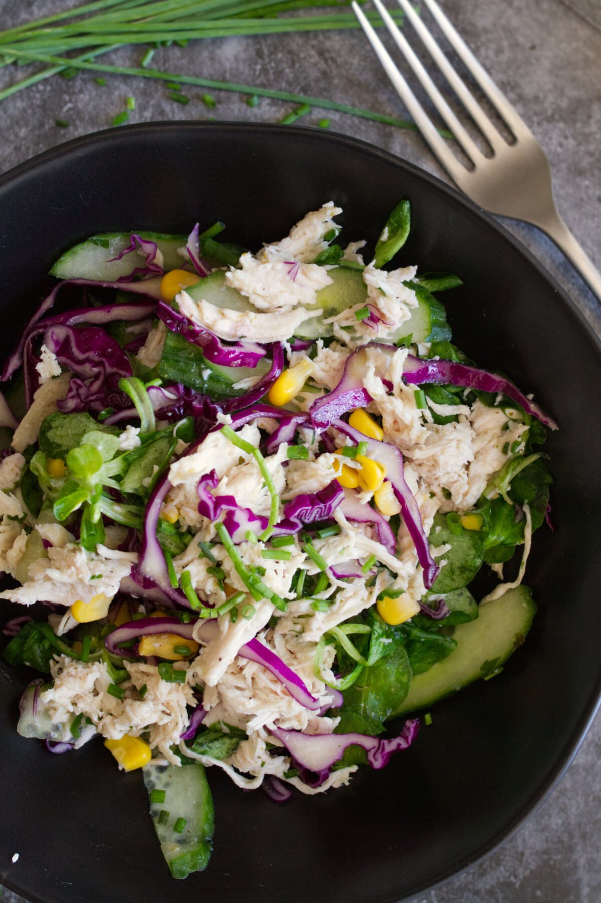 A bowl of shredded chicken salad sits beside a fork.