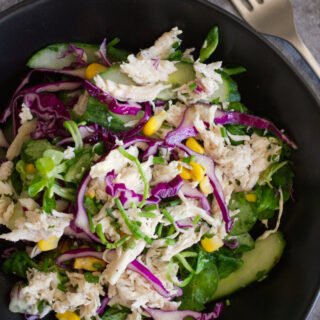 A bowl of shredded chicken salad sits beside a fork.