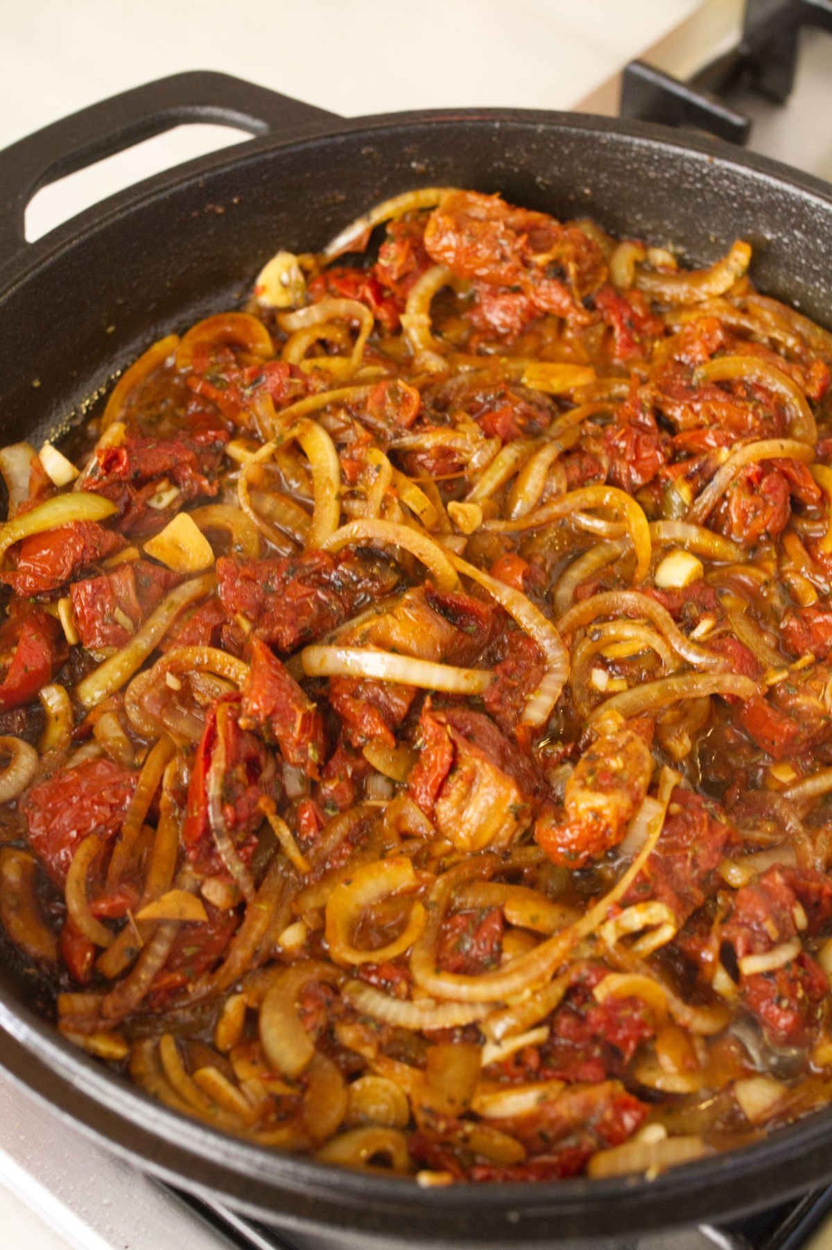 A pan of sun dried tomatoes, garlic, onion simmer with herbs and spices. 