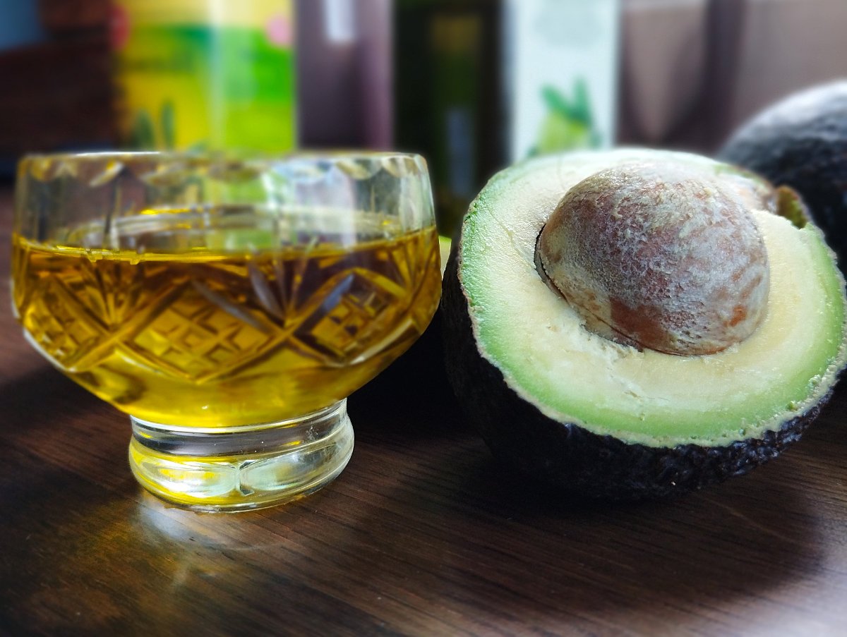 A small glass of olive oil sits beside an avocado cut in half. 